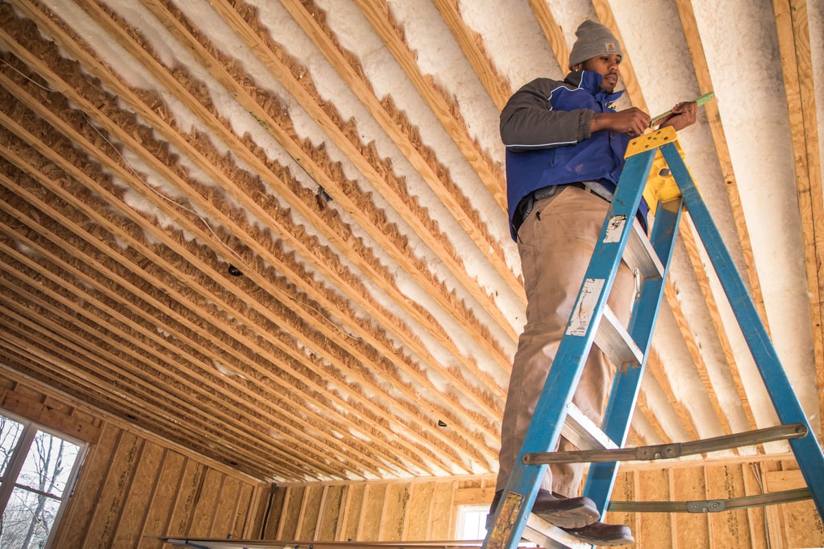 ESG technician on a ladder inspecting open ceiling framing and insulation