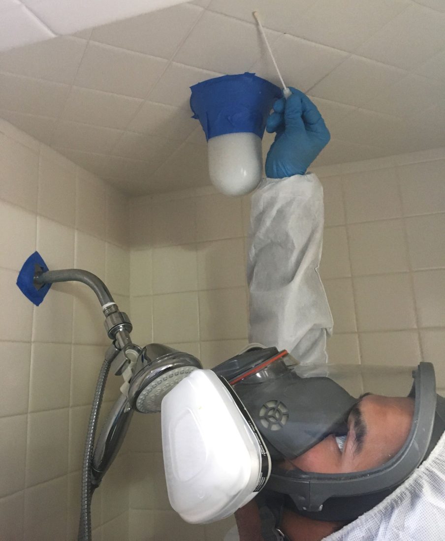 Technician in protective equipment inspecting a ceiling area with a light