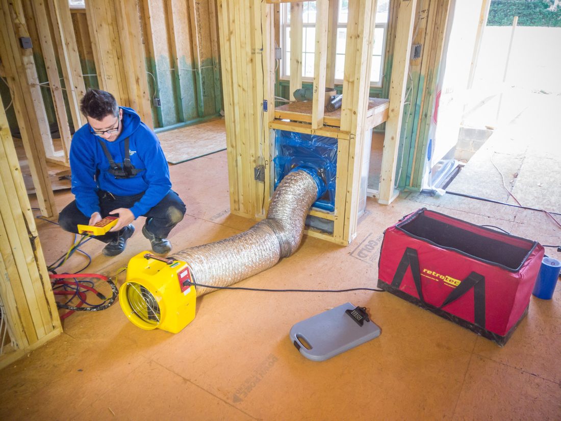 ESG inspector in protective equipment collecting a floor-level air sample inside a North Carolina home